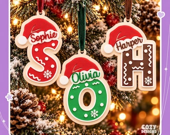 May include: Three personalized Christmas ornaments shaped as letters S, O, and H, each topped with a red Santa hat. The letters are red, green, and brown with white snowflake and squiggle details. Each ornament features a name: Sophie, Olivia, or Harper.