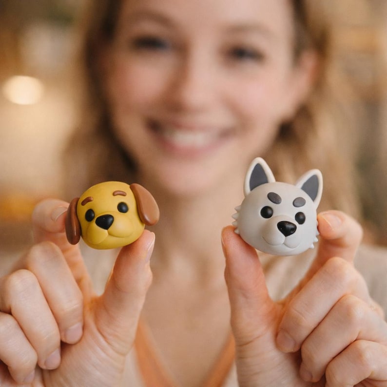 K&ouml;nnte beinhalten: Zwei kleine, hundef&ouml;rmige Figuren. Eine ist gelb mit braunen Ohren, die andere grau mit schwarzen Akzenten. Beide haben schwarze Augen und Nasen, vor einem unscharfen Hintergrund.
