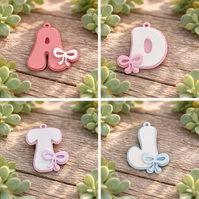 May include: Four individual letter charms featuring the letters A, D, T, and J. Each letter has a rounded, puffy design with a small attached bow detail. The letter A is coral, D is white with a pink border, T is white with a pink border, and J is white with a light blue border.