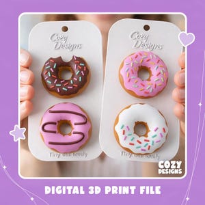 Op de afbeelding: Twee witte rechthoekige displaykaarten met het label Cozy Designs en Tiny but lovely, elk met twee miniatuur donutmodellen. Eén kaart toont een donut met chocoladeglazuur en hagelslag en een roze donut met strepen. De andere toont een roze donut met hagelslag en een witte donut met hagelslag.