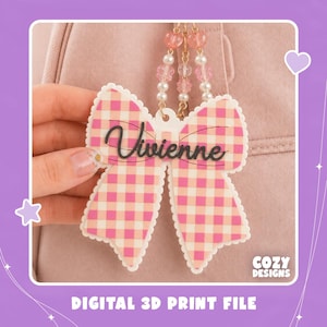 Könnte beinhalten: Ein schleifenförmiger Acryl-Anhänger mit rosa-weißem Vichy-Muster und dem Namen Vivienne in schwarzer Schreibschrift. Der Anhänger ist an einer goldfarbenen Kette befestigt, die mit rosa herzförmigen Perlen, klaren blütenförmigen Perlen und weißen Perlen verziert ist.