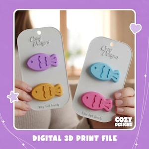 May include: Two white rectangular display cards featuring the text Cozy Designs and Tiny but lovely. Each card holds two fish-shaped items. The left card has a purple and a yellow fish. The right card has a light blue and a pink fish.