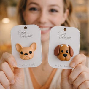 K&ouml;nnte beinhalten: Zwei Hunde-Accessoires auf wei&szlig;en Karten. Einer ist eine hellbraune franz&ouml;sische Bulldogge, der andere ein braun-wei&szlig; gefleckter Hund. Auf den Karten steht "Cozy Designs" und "Tiny but lovely."