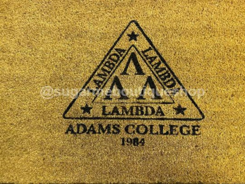 May include: A gold doormat with a black triangle design featuring the text "Lambda Adams College 1984".