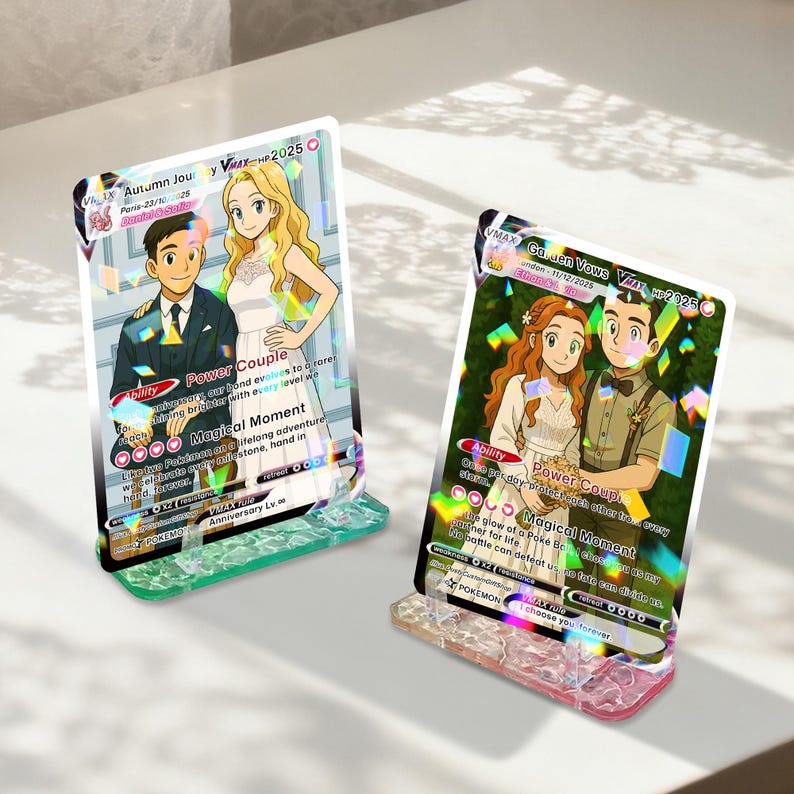 May include: Two Pokemon card displays showing couples in wedding outfits. The cards have holographic details and are set in clear acrylic stands with coloured bases. Text includes "Power Couple" and "Magical Moment."
