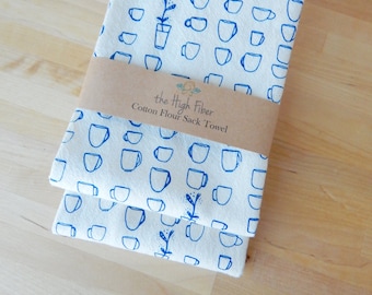 May include: Two white cotton flour sack towels with a blue coffee cup pattern. The towels are folded and have a brown label that reads "the High Fiber Cotton Flour Sack Towel".