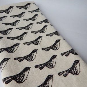 May include: A white fabric tea towel with a repeating pattern of black stylized birds. The birds are facing right and have a simple design.