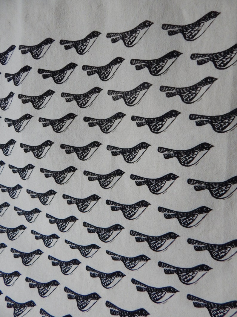 May include: A white fabric tote bag with a black and white repeating pattern of birds flying in a diagonal line. The birds are stylized and have a simple design.