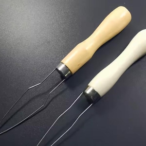 May include: Two seam rippers with wooden handles. One handle is light-coloured wood, the other is white. The metal blades are silver and have a pointed tip. The tools are designed for removing stitches from fabric.