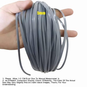 May include: A coil of gray, flexible material, approximately 5mm in width, is held in a hand. The text "5mm" is visible. The material appears to be a type of cord or trim, suitable for various crafting or DIY projects.