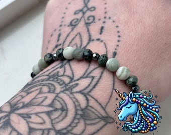 May include: A green and black beaded bracelet with a mandala tattoo on the wearer's arm. The bracelet is made with green and black beads and has a silver clasp. The tattoo is a black mandala design. The bracelet is from the Unicorn Beading Company.