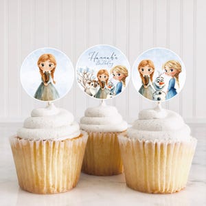 Puede incluir: Tres cupcakes con glaseado blanco y adornos decorativos con ilustraciones de acuarela de personajes de una popular pel&iacute;cula de animaci&oacute;n. Un adorno tiene el texto "Hannah's Birthday". Los cupcakes est&aacute;n en moldes de papel blancos.