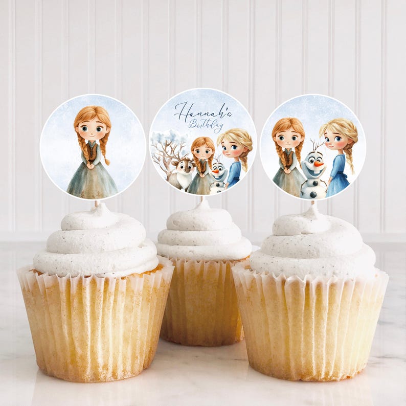 Puede incluir: Tres cupcakes con glaseado blanco y adornos decorativos con ilustraciones de acuarela de personajes de una popular pel&iacute;cula de animaci&oacute;n. Un adorno tiene el texto "Hannah's Birthday". Los cupcakes est&aacute;n en moldes de papel blancos.