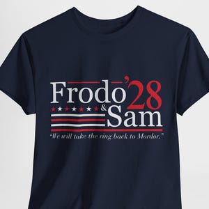 May include: A navy blue t-shirt with a white and red graphic design. The graphic features the text "Frodo '28 & Sam" with a red, white, and blue striped design and stars. The text "We will take the ring back to Mordor." is printed below the graphic.