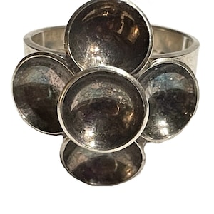 May include: A silver ring with five round, slightly concave, silver discs arranged in a flower shape.