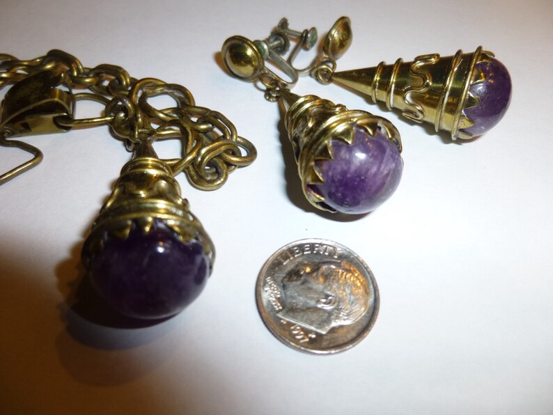 May include: A pair of gold-tone clip-on earrings with purple amethyst stones. The earrings feature a cone-shaped design with a wire-wrapped detail.