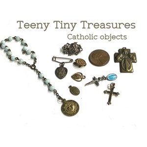 May include: A collection of small Catholic religious objects, including a rosary, a cross, a pin, and several medallions. The objects are arranged on a white background. The text "Teeny Tiny Treasures Catholic objects" is displayed above the objects.
