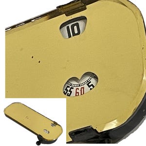 May include: A vintage gold-toned timer with a black border. The timer features a dial with numbers 55, 60, and 5, and a separate window displaying the number 10. The timer is rectangular with rounded edges.