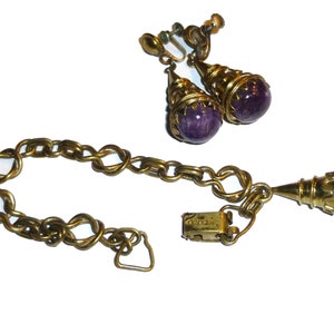 May include: A vintage jewellery set comprising a gold chain bracelet and a pair of earrings with purple stone accents. The earrings are clip-on style and the bracelet has a clasp closure.