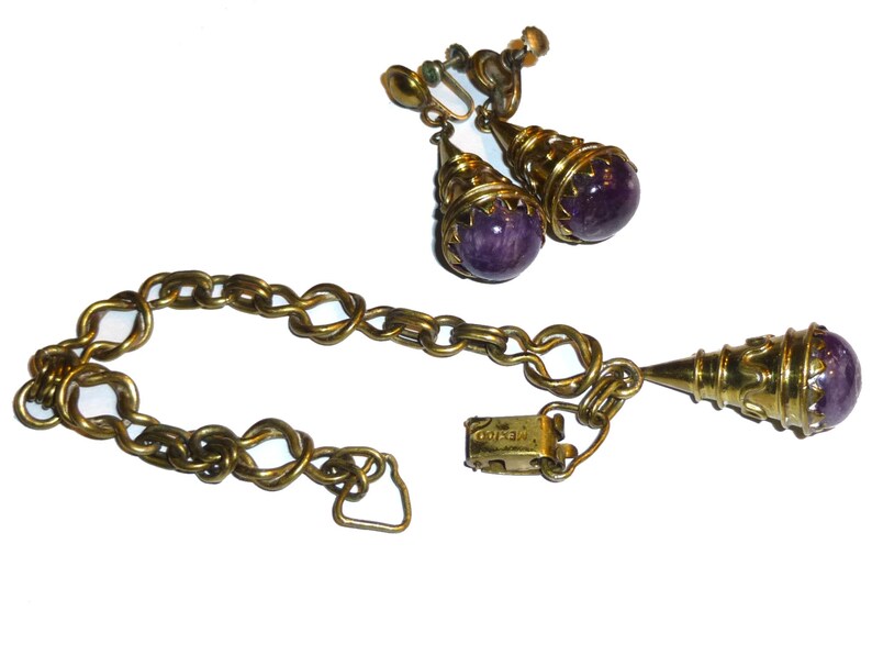 May include: A vintage jewellery set comprising a gold chain bracelet and a pair of earrings with purple stone accents. The earrings are clip-on style and the bracelet has a clasp closure.