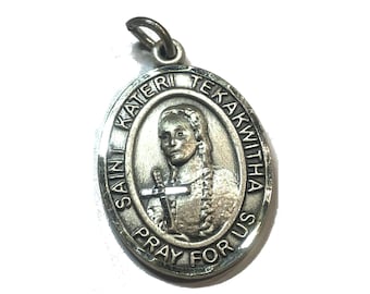 May include: Silver oval medal with a raised image of Saint Kateri Tekakwitha, a Native American woman holding a cross. The medal is inscribed with "Saint Kateri Tekakwitha Pray For Us".