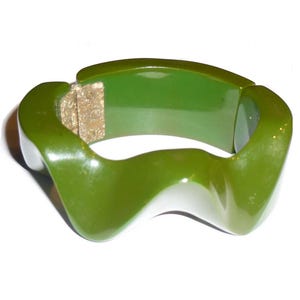 May include: A green plastic bangle bracelet with a wavy, abstract design. The bracelet is open and has a gold-colored clasp.