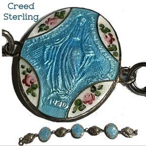 May include: A sterling silver bracelet featuring oval links with blue enamel depictions of the Virgin Mary and white enamel sections decorated with pink roses and green leaves. The text Creed Sterling is visible in the upper left corner.