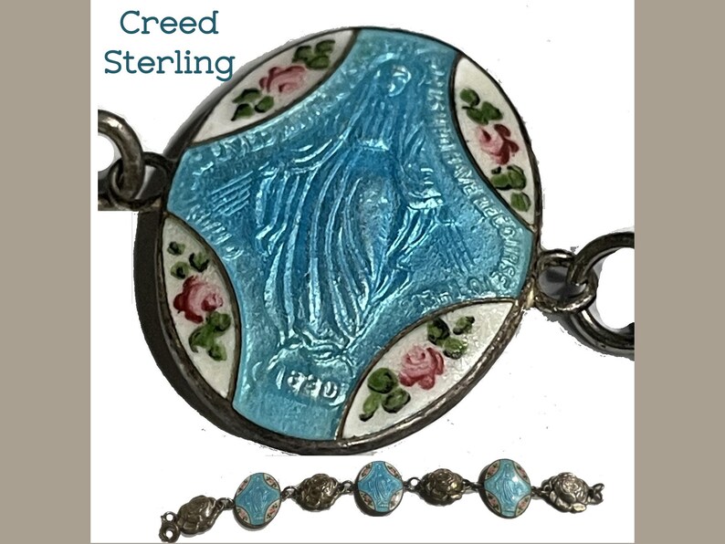 May include: A sterling silver bracelet featuring oval links with blue enamel depictions of the Virgin Mary and white enamel sections decorated with pink roses and green leaves. The text Creed Sterling is visible in the upper left corner.