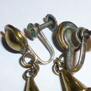 May include: A pair of gold tone clip-on earrings with a cone-shaped dangle. The earrings have a screw-on back closure.