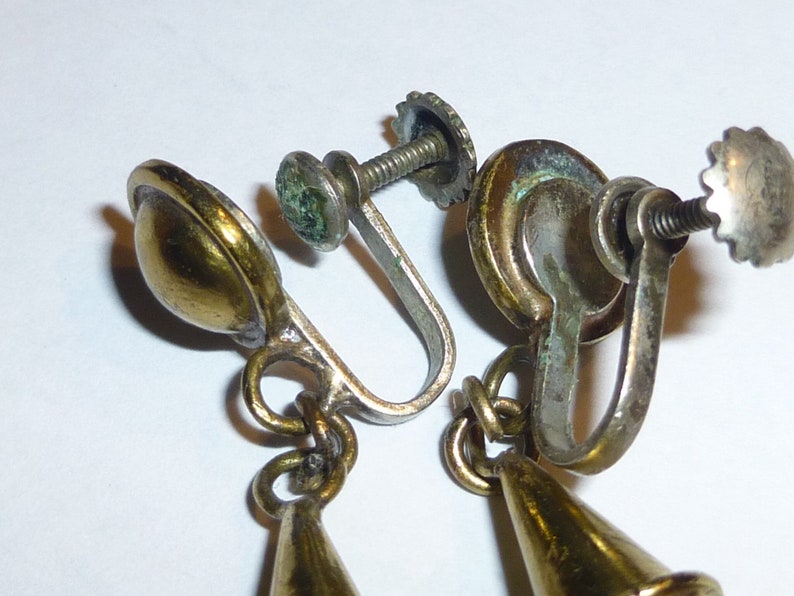 May include: A pair of gold tone clip-on earrings with a cone-shaped dangle. The earrings have a screw-on back closure.