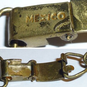 May include: A gold-coloured metal clasp with a hinged opening. The clasp has the word "MEXICO" engraved on it.