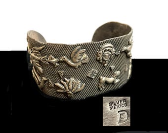 May include: Silver cuff bracelet with a textured surface and embossed designs of birds, animals, and a human figure. The bracelet is stamped "SILVER MEXICO" and has a letter "D" on the back.
