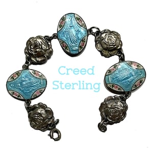 May include: A sterling silver bracelet featuring three oval-shaped charms with light blue enamel and a central figure, alternating with four silver rose-shaped links. The text Creed Sterling is printed in light blue in the centre of the image.