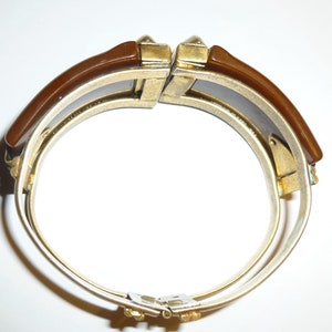 May include: A brown and silver hinged bangle bracelet with a decorative design on the clasp.