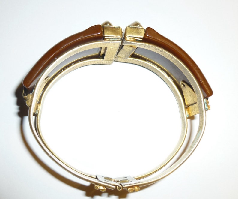 May include: A brown and silver hinged bangle bracelet with a decorative design on the clasp.