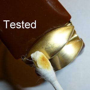 May include: Close-up of a brown and gold lighter with a cotton swab dipped in a brown substance. The lighter has the word "Tested" written on it.