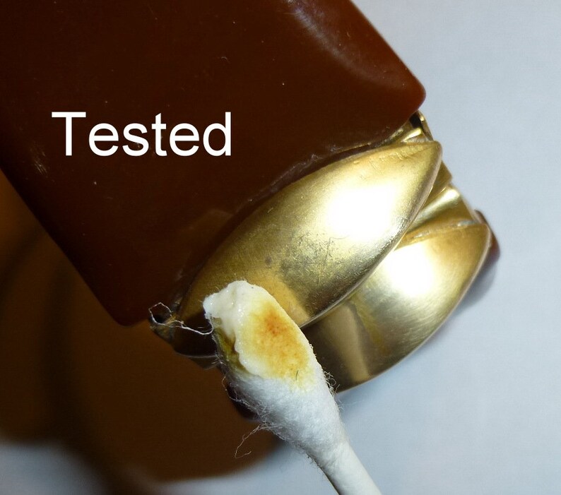 May include: Close-up of a brown and gold lighter with a cotton swab dipped in a brown substance. The lighter has the word "Tested" written on it.