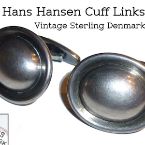 May include: A pair of silver cuff links with a rounded, domed design. The cuff links are marked "HH 925S DENMARK".