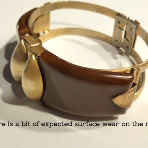 May include: A brown and gold bangle bracelet with a hinged clasp. The bracelet has a smooth, rounded shape and a simple design.