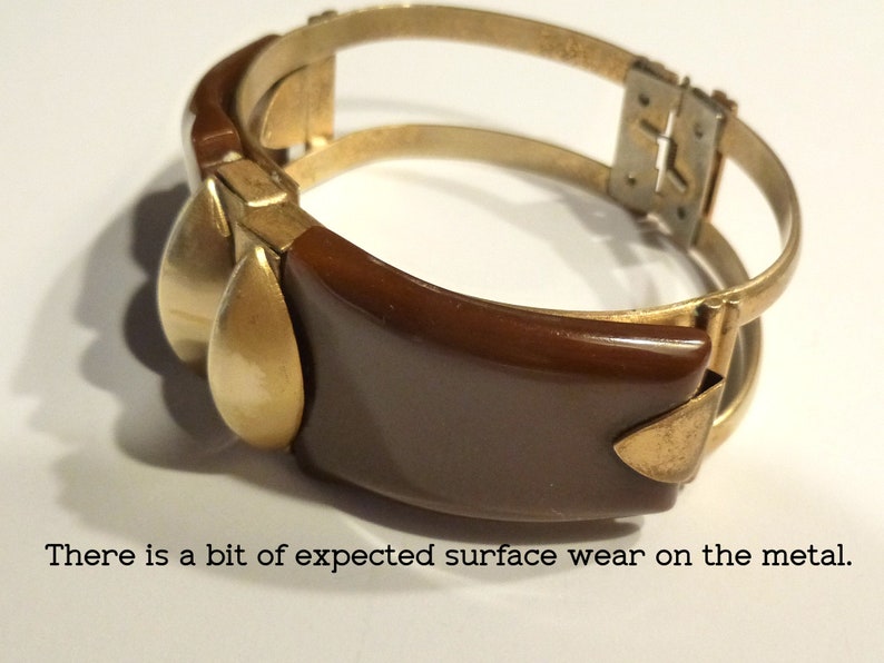 May include: A brown and gold bangle bracelet with a hinged clasp. The bracelet has a smooth, rounded shape and a simple design.