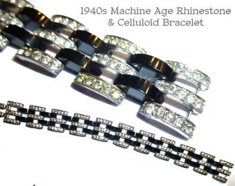 May include: A black and silver bracelet with a geometric design. The bracelet is made of celluloid and features a row of rhinestones.