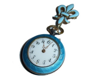 May include: A blue enamel pocket watch with a fleur-de-lis design on the top. The watch face has Roman numerals and black hands.