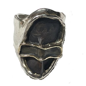 May include: A silver ring with a black stone set in a textured silver band. The stone is surrounded by a thin gold band.