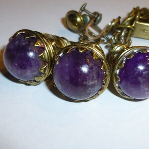 May include: A set of three amethyst earrings with gold-tone metal settings. The earrings are marked "Mexico".