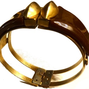 May include: A brown and gold hinged bangle bracelet with a decorative design. The bracelet is made of metal and has a hinge closure.