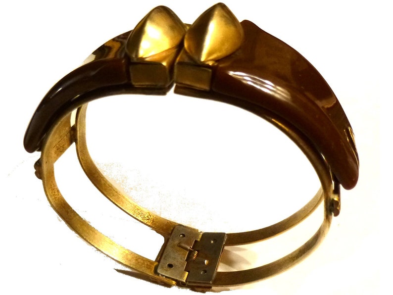 May include: A brown and gold hinged bangle bracelet with a decorative design. The bracelet is made of metal and has a hinge closure.