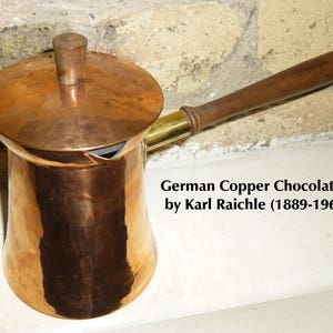May include: A copper chocolate pot with a wooden handle and a lid. The pot is made by Karl Raichle (1889-1965).