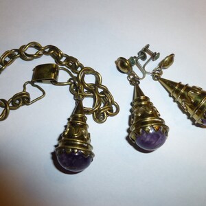 May include: A set of gold-tone jewellery with purple amethyst stones. The set includes a bracelet and a pair of earrings.