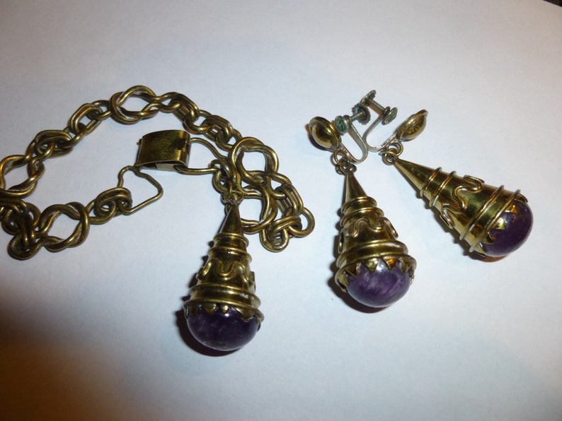 May include: A set of gold-tone jewellery with purple amethyst stones. The set includes a bracelet and a pair of earrings.