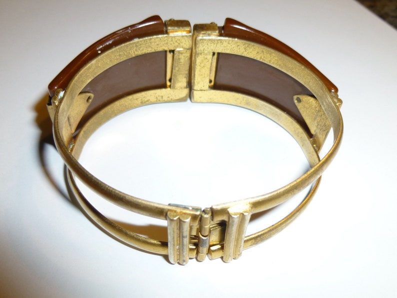 May include: A gold-toned bangle bracelet with a brown plastic insert. The bracelet is hinged and has a double band design.